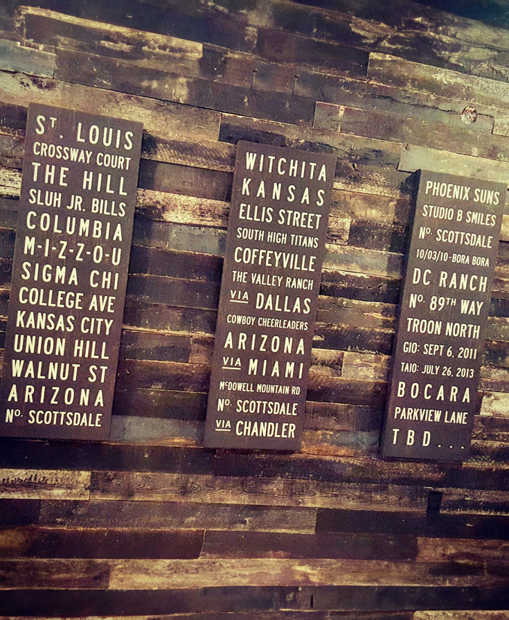 A set of three custom subway signs by Transit Design hanging on a rustic wall.