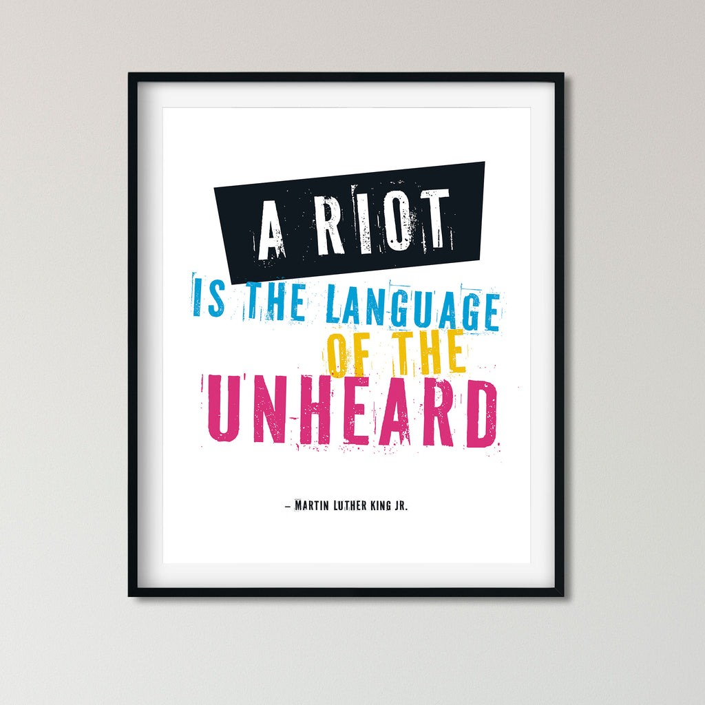 A framed typographic wall art print featuring the quote 'A RIOT IS THE LANGUAGE OF THE UNHEARD' attributed to Martin Luther King Jr., with bold white, blue, yellow, and pink lettering on a white background and a black frame.