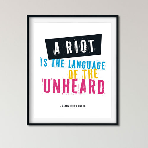 A framed typographic wall art print featuring the quote 'A RIOT IS THE LANGUAGE OF THE UNHEARD' attributed to Martin Luther King Jr., with bold white, blue, yellow, and pink lettering on a white background and a black frame.