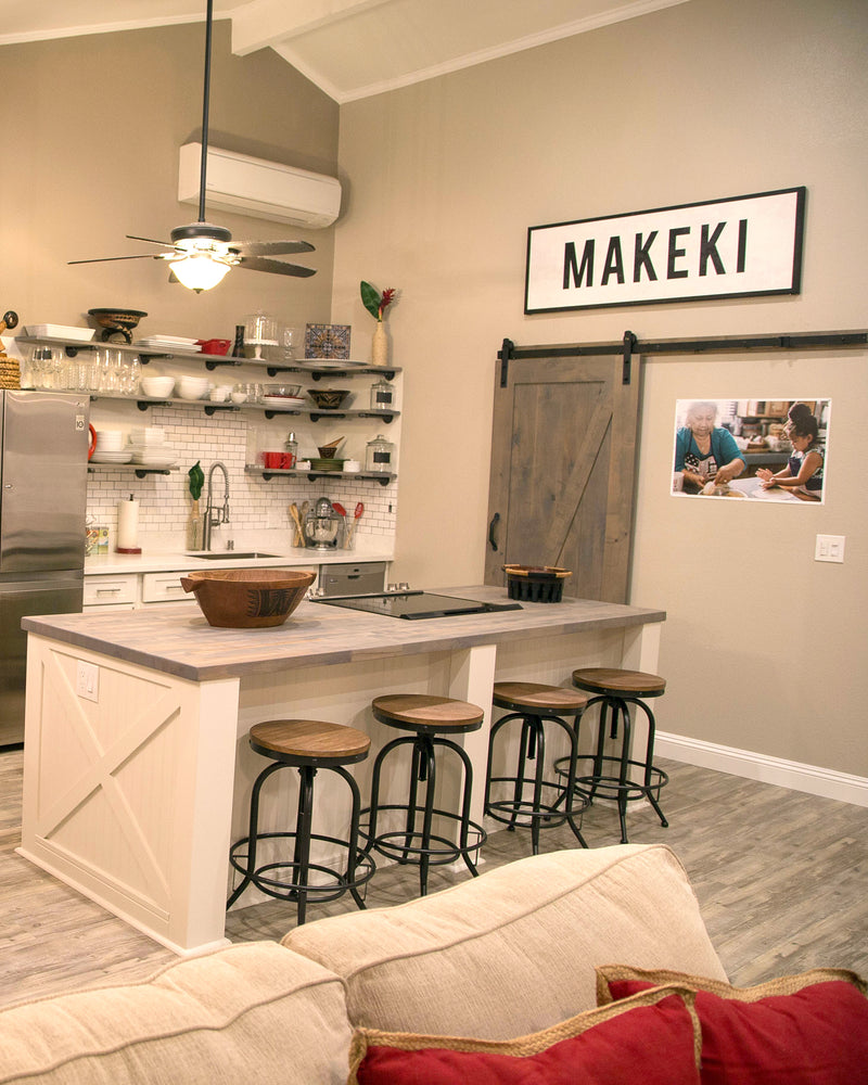 Modern kitchen with island, stools, with custom farmhouse sign that says 'MAKEKI' on wall, from Transit Design.