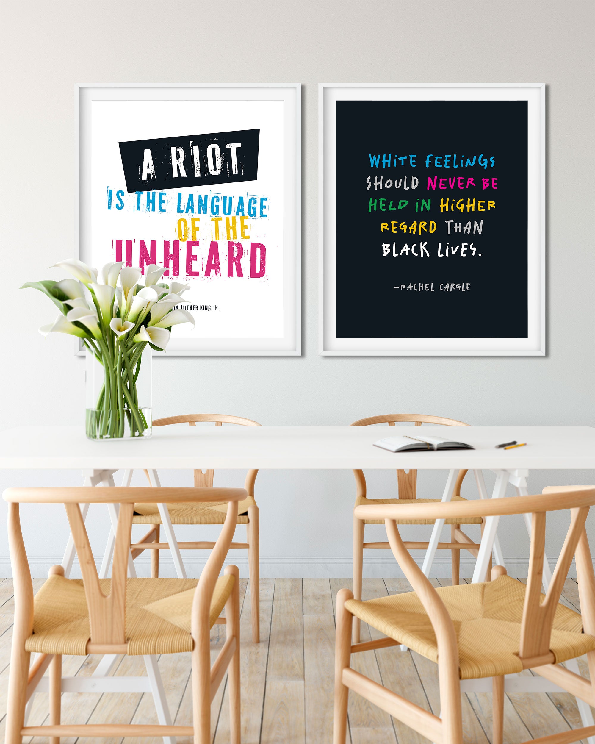 Two framed social justice posters displayed above a dining table in a bright, modern room. The left print has a white background with black and colorful text reading 'A RIOT IS THE LANGUAGE OF THE UNHEARD', by Martin Luther King Junior.