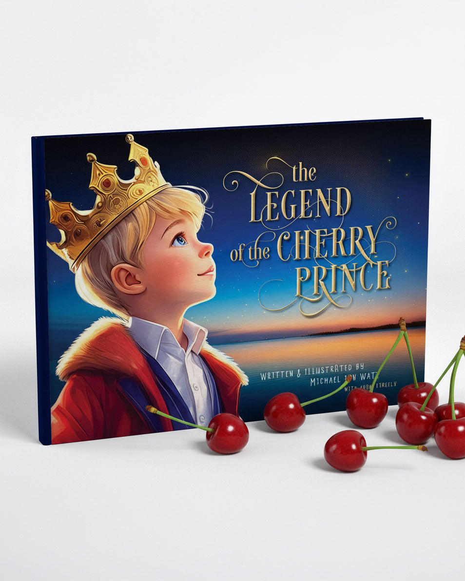 A children's book titled "The Legend of the Cherry Prince" stands upright on a white surface with several red cherries placed in front. The cover shows an illustrated blond boy wearing a gold crown and a red coat against a dark blue sky background.